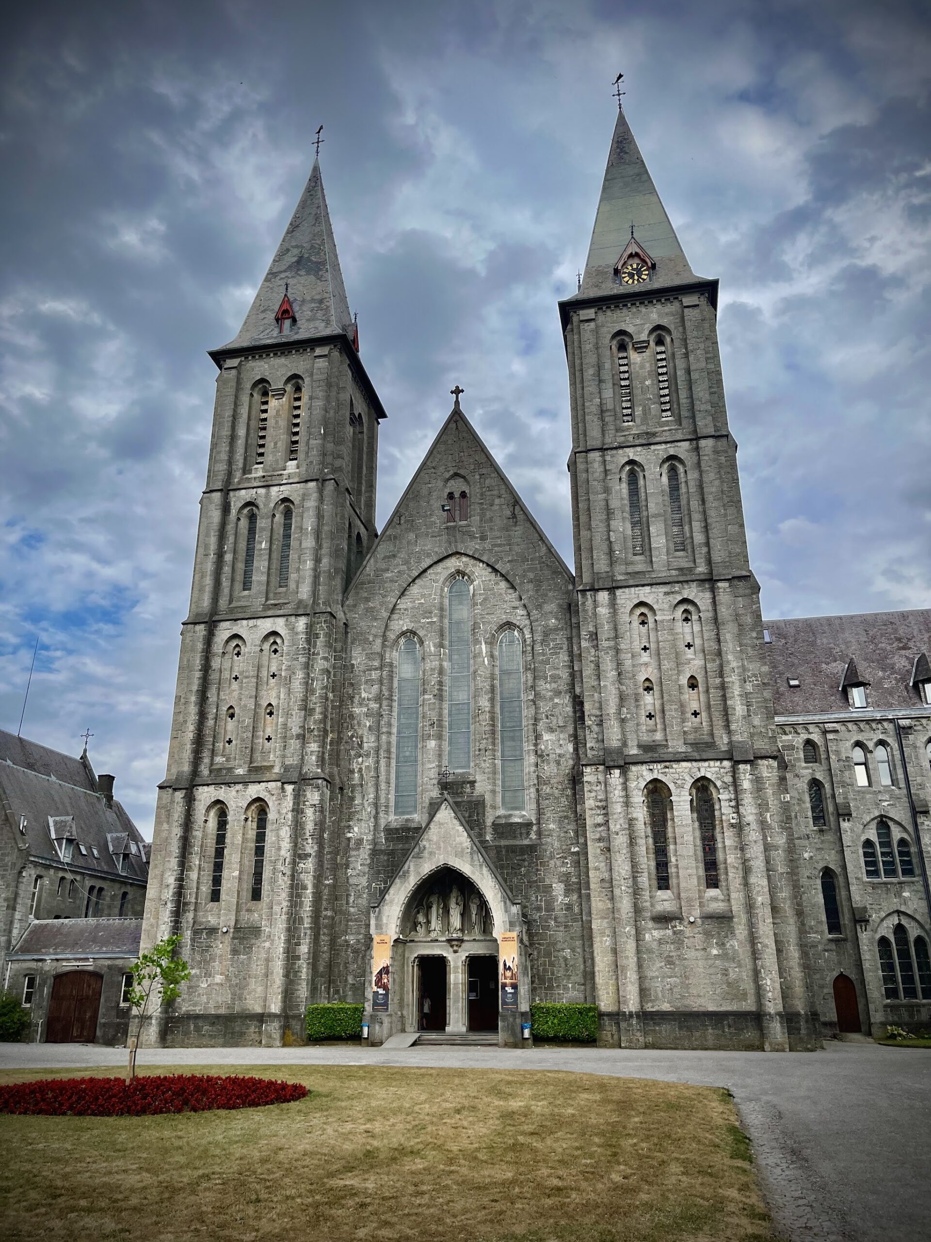 La façade néogothique de l’abbaye de Maredsous et ses deux flèches sous un ciel nuageux