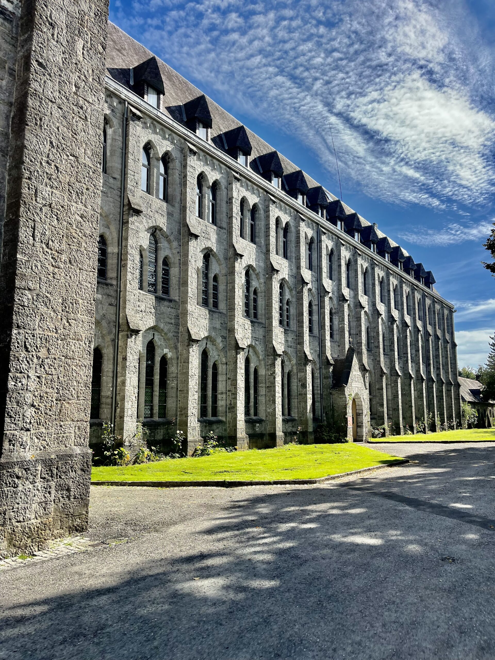 Longue façade de pierre de l’abbaye de Maredsous sous un ciel bleu